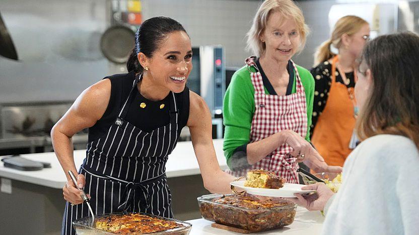 Meghan Markle smiles while serving lunch to a woman